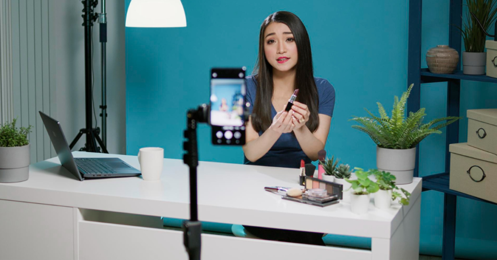 A female content creator, engaging in influencer marketing, films a product review in a studio setting, showcasing makeup products on camera.